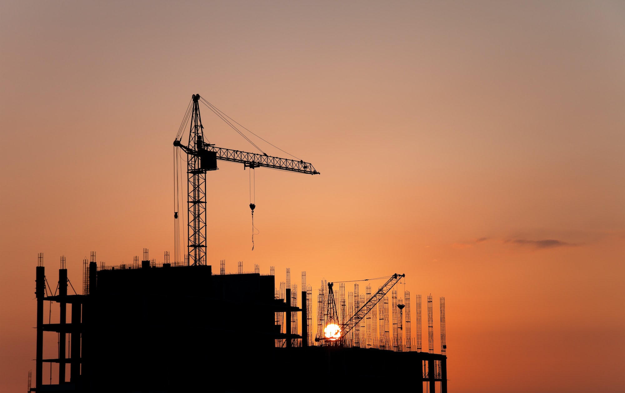 Construction cranes and concrete structure at sunset